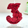 A red glitter bow number candle shaped like the number 3, used for birthday and celebration cakes.