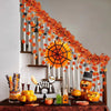 An artificial maple leaf garland hanging vine decorated with orange and black elements against a white wall.