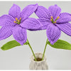 Hand-crocheted purple lily flowers with green leaves displayed in a white vase