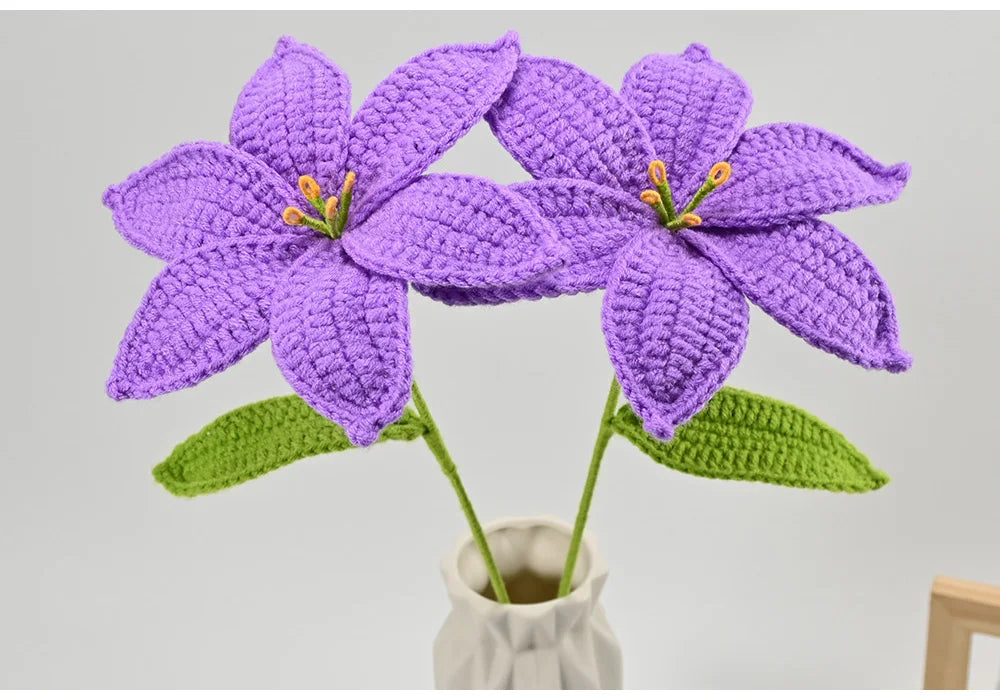Hand-crocheted purple lily flowers with green leaves displayed in a white vase