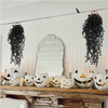 A display of carved pumpkin decorations and artificial black vine hanging plants on a rustic wooden surface.