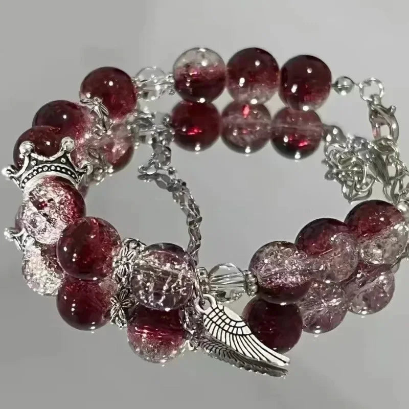 A bracelet made of deep red and pink translucent natural stones, featuring a crown charm and an angel wing pendant.