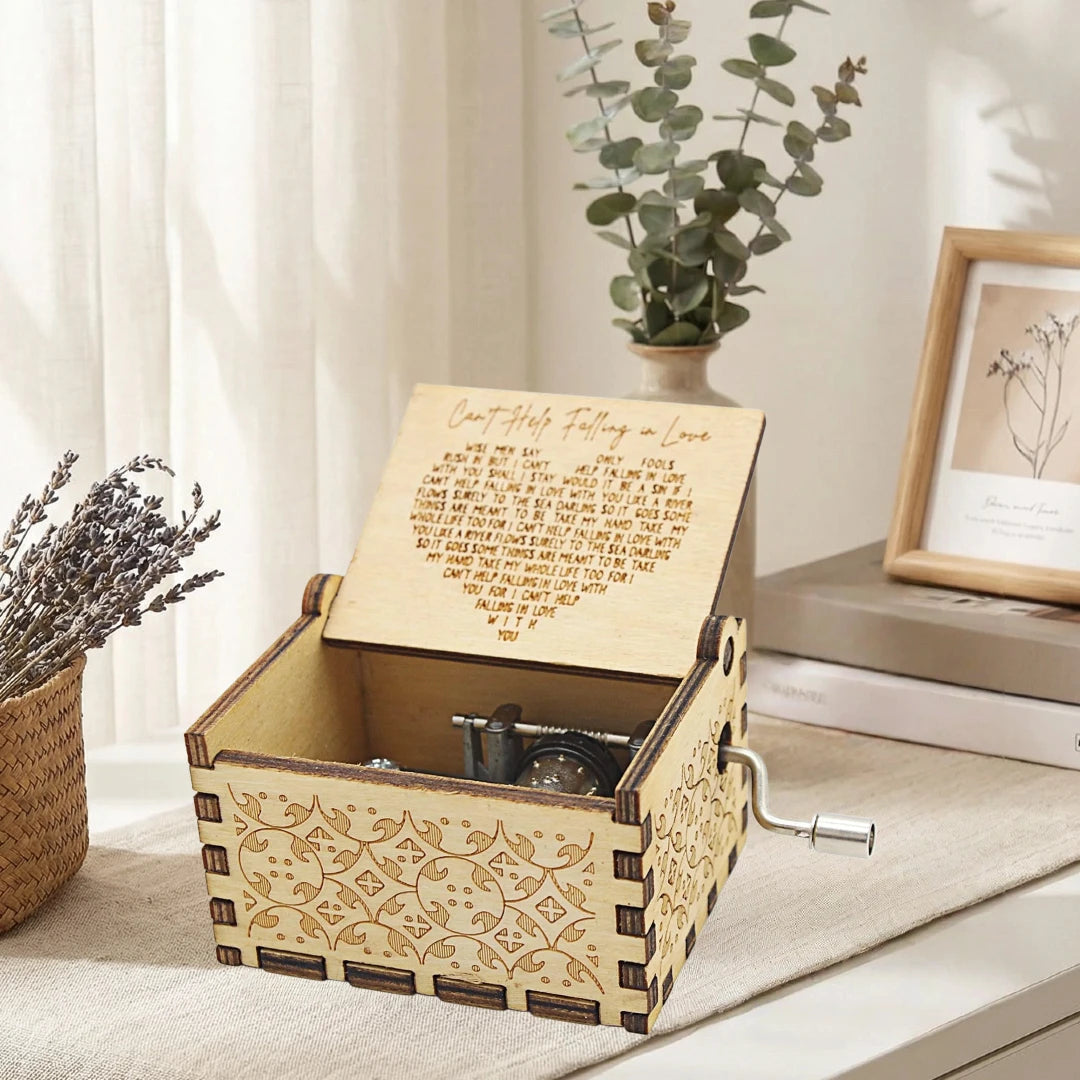 An antique wood music box with an engraved melody sits on a light surface next to a potted plant.