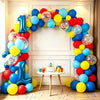 A colorful arch garland made of balloons in blue, yellow, and red surrounds a white wall for a party decoration.
