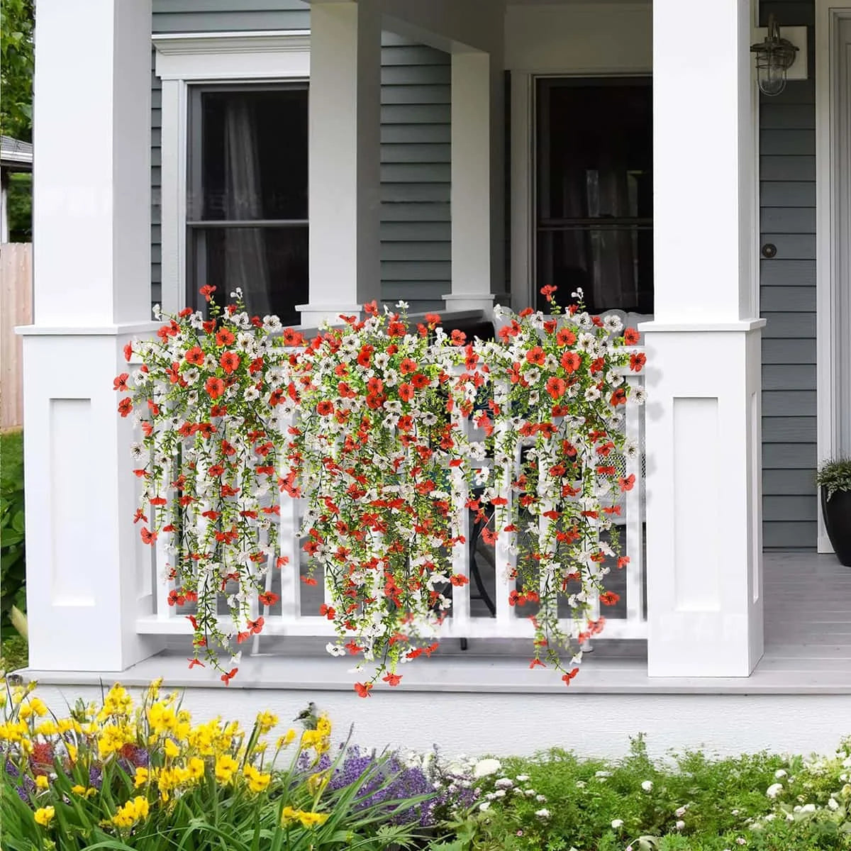 A white porch railing decorated with cascading red and white faux silk flowers in a garden setting.