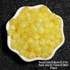 A pile of 50 clear yellow glitter resin beads for jewelry making with a specified size and hole diameter.