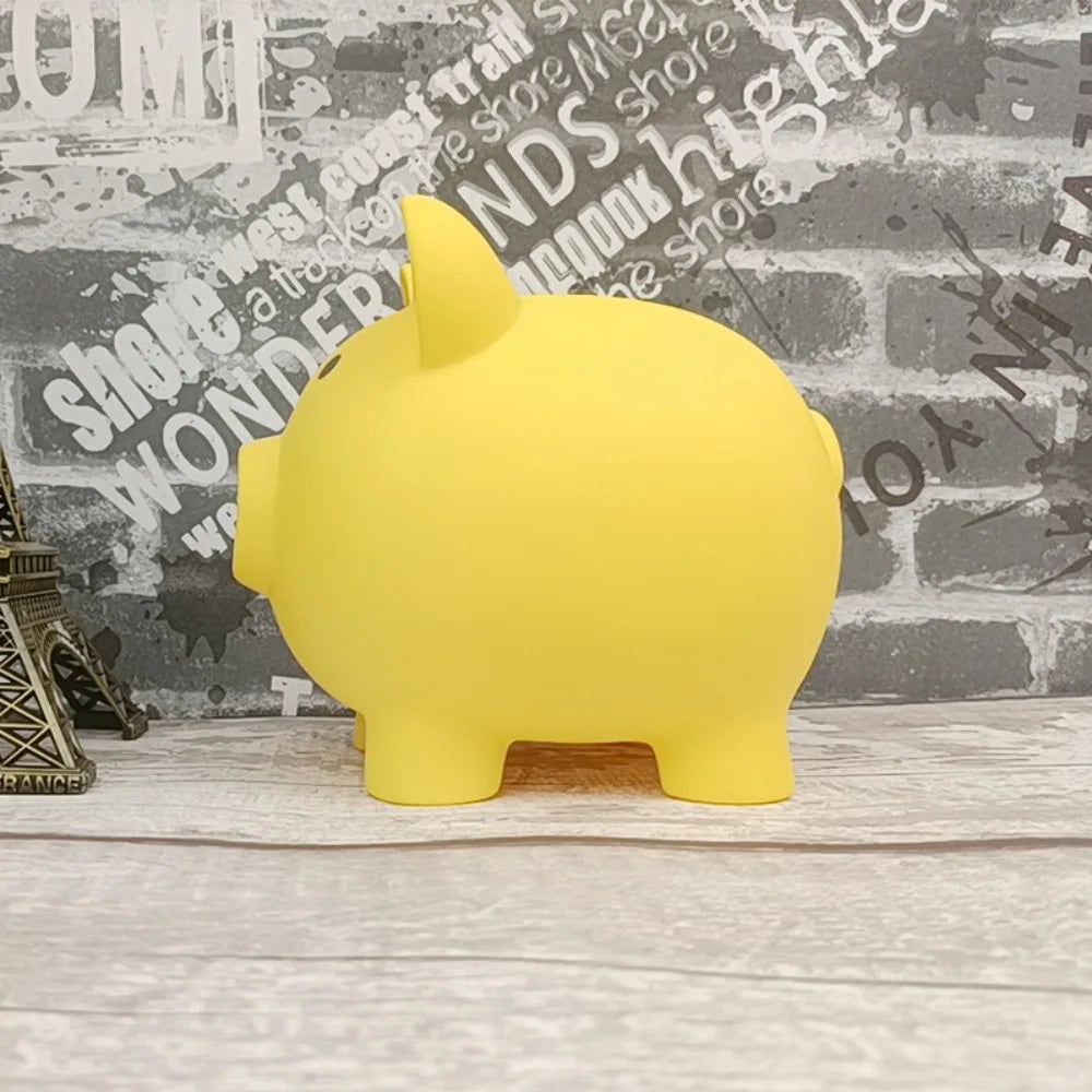A bright yellow pig-shaped coin storage bank sitting on a light wooden surface against a textured gray brick wall.