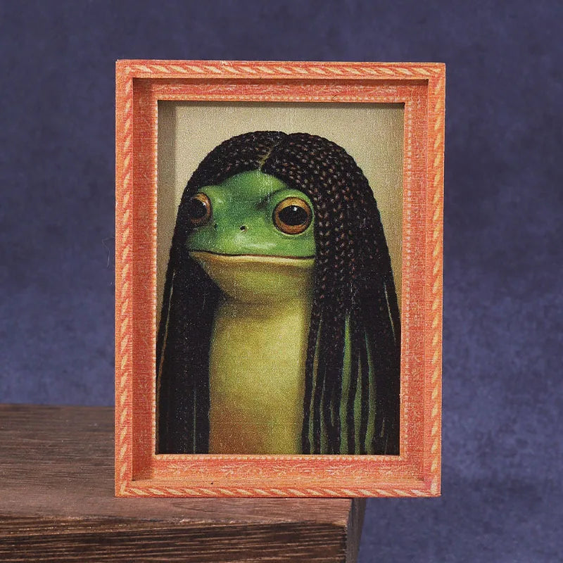A framed picture of a green frog with long black hair, displayed in a wooden photo frame.