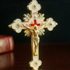 Elegant gold metal Jesus cross ornament with a red center and decorative rays.