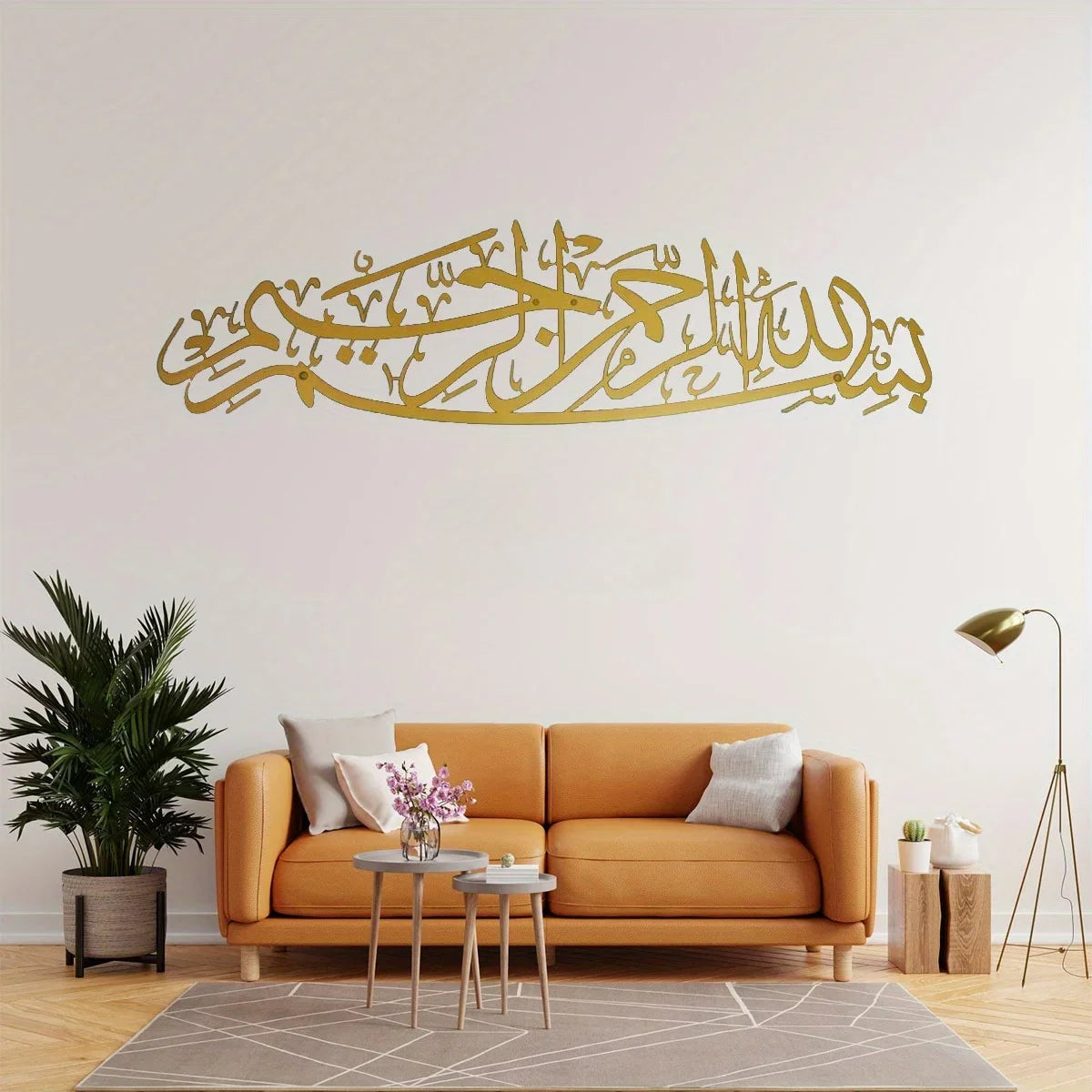 Gold metal calligraphy art featuring the Bismillah written on a white wall above an orange sofa.