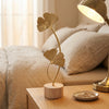A gold-toned iron ginkgo leaf ornament set standing on a wooden surface next to a lamp.