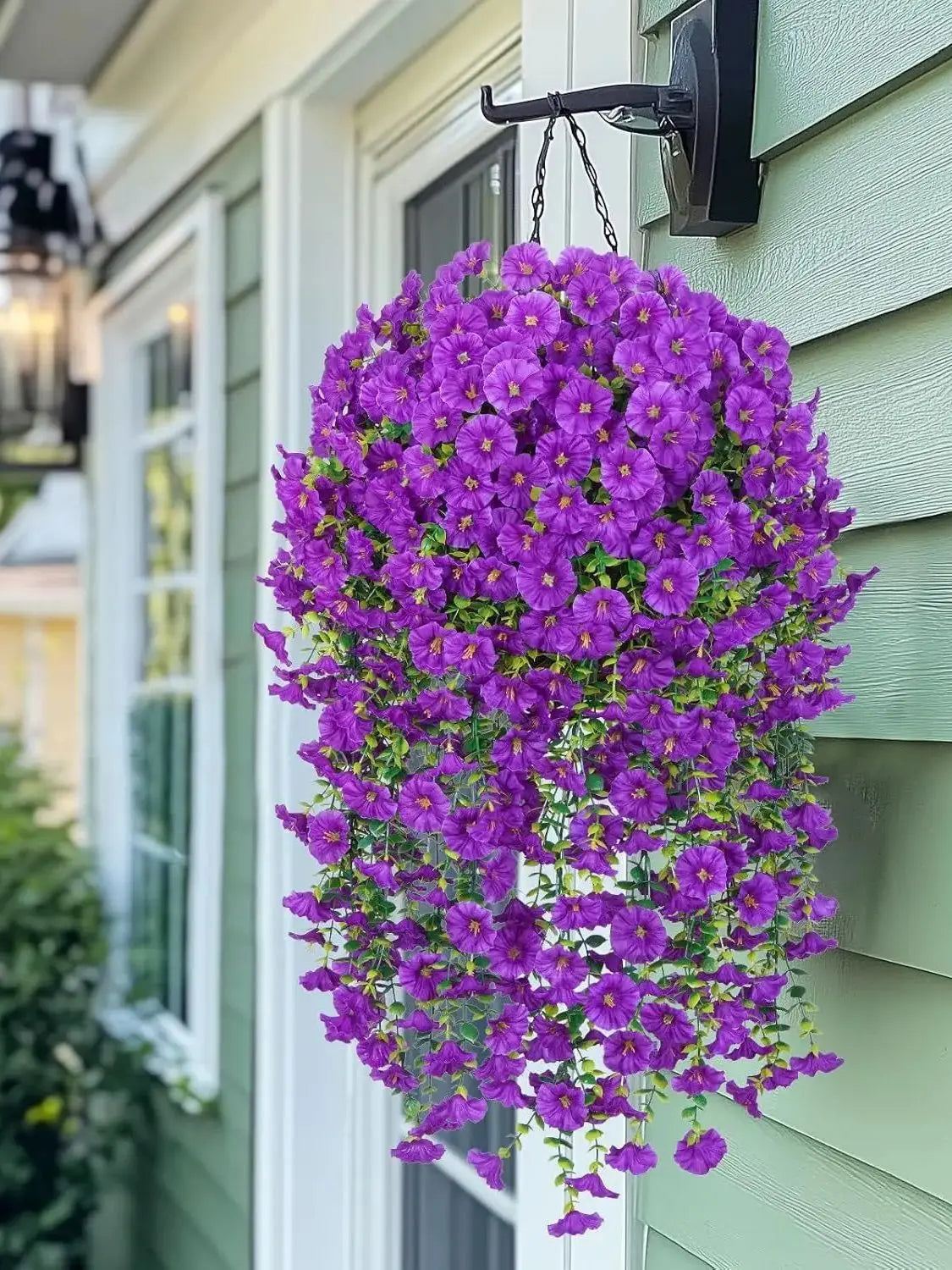 A vibrant purple artificial morning glory hanging vine cascading down a light green siding wall.