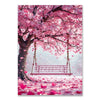 A pink cherry blossom tree with a wooden swing hangs over a field covered in pink petals.