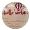 A natural wood birth announcement plaque featuring a red hot air balloon, clouds, and text that reads hello world.
