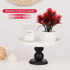 Un faux bonsaï rouge vif dans un pot blanc, exposé sur un socle blanc avec une bougie en verre.