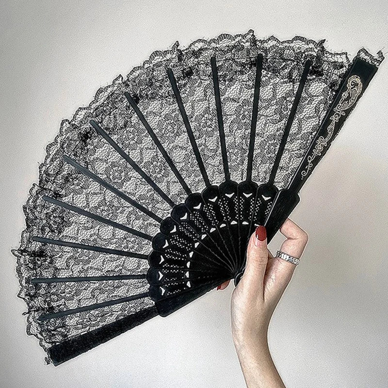 A hand holding an elegant black lace folding fan with a scalloped edge and decorative accents.