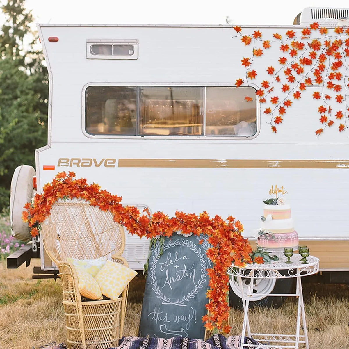 A white RV is decorated with an orange artificial maple leaf garland hanging vine and a rustic wooden sign.