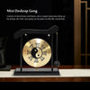 A small brass gong suspended by strings on a wooden frame, resting on a dark surface.