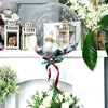 A clear inflatable glass sphere filled with decorative elements and a ribbon, displayed on a white mantelpiece.