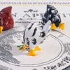 A set of three ceramic chicken figures in red, black, and white are displayed on a patterned cloth.