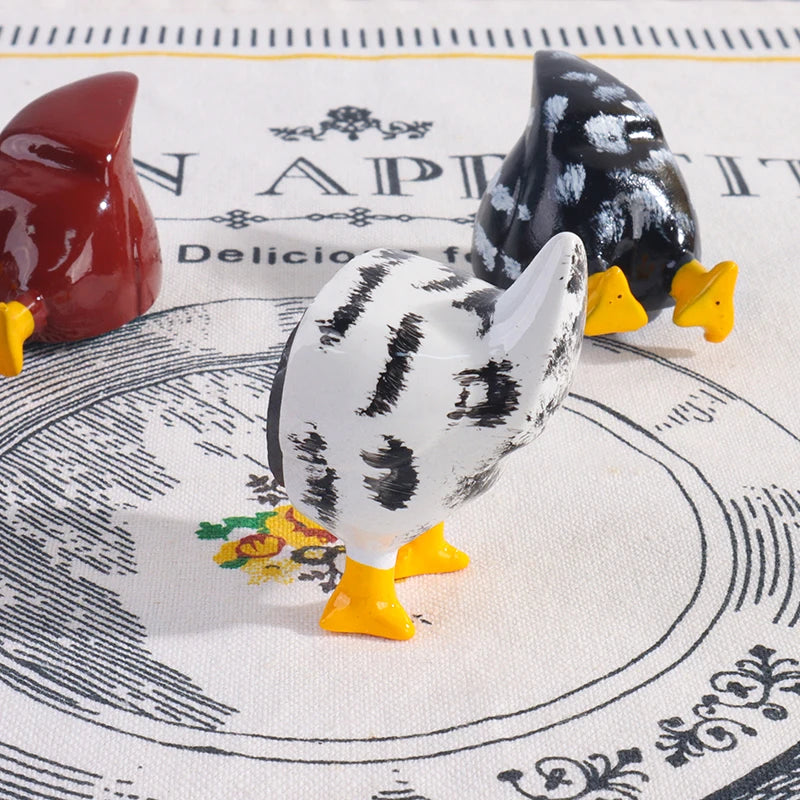 A set of three ceramic chicken figures in red, black, and white are displayed on a patterned cloth.
