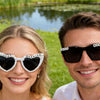 A smiling bride and groom wearing pearl decor glasses for wedding photos outdoors.