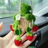 Hand-knitted hanging plant basket decor featuring green leaves and white flowers, displayed in a hand.