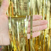A hand holds vertical strands of metallic gold tinsel foil fringe curtain backdrop for parties.