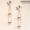 Two decorative glass terrariums featuring white and blue bird-like figurines suspended by twine.