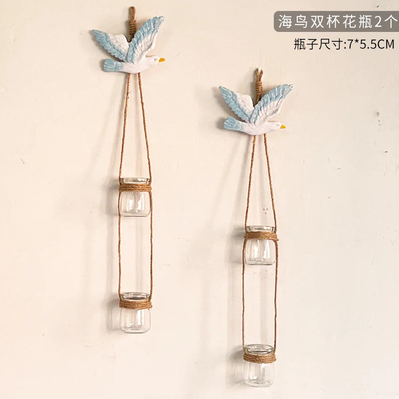 Two decorative glass terrariums featuring white and blue bird-like figurines suspended by twine.