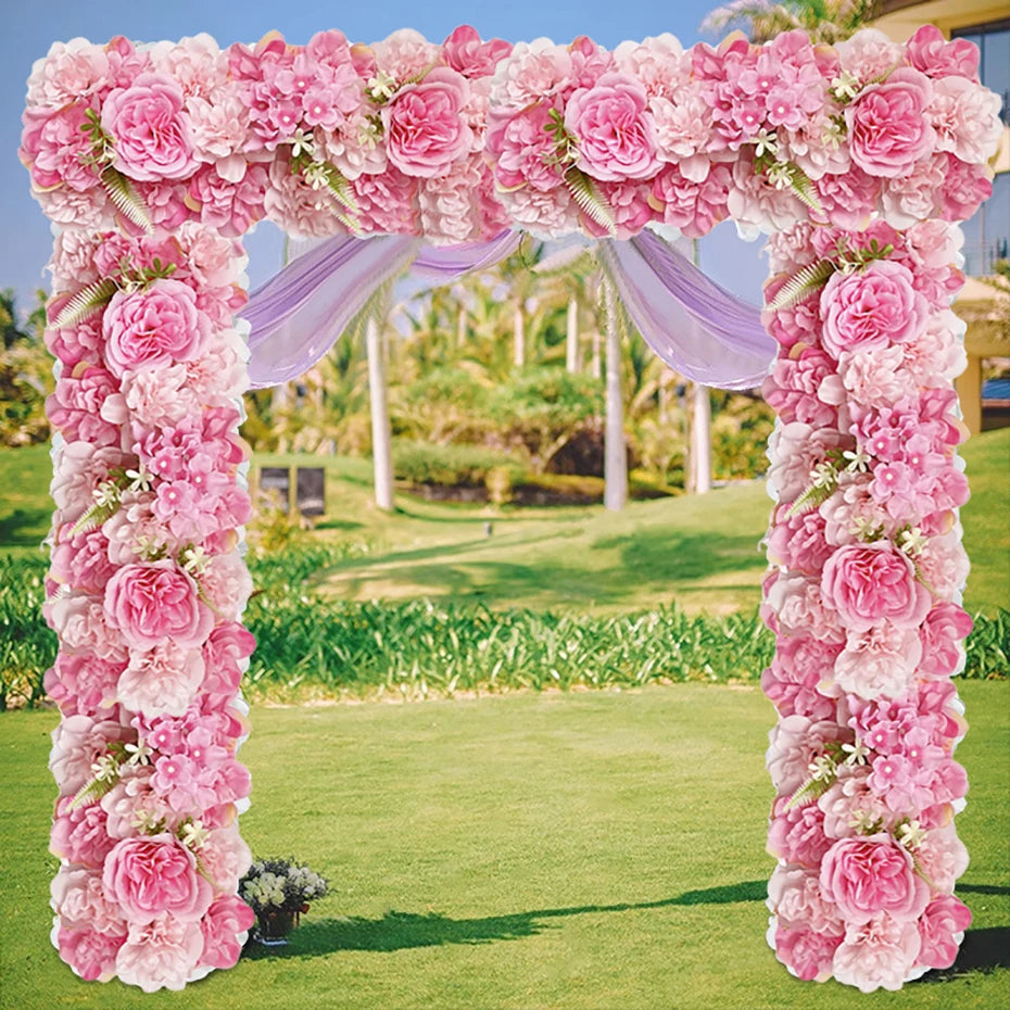 A floral archway made of pink and white artificial silk roses for weddings and events in a green outdoor setting.