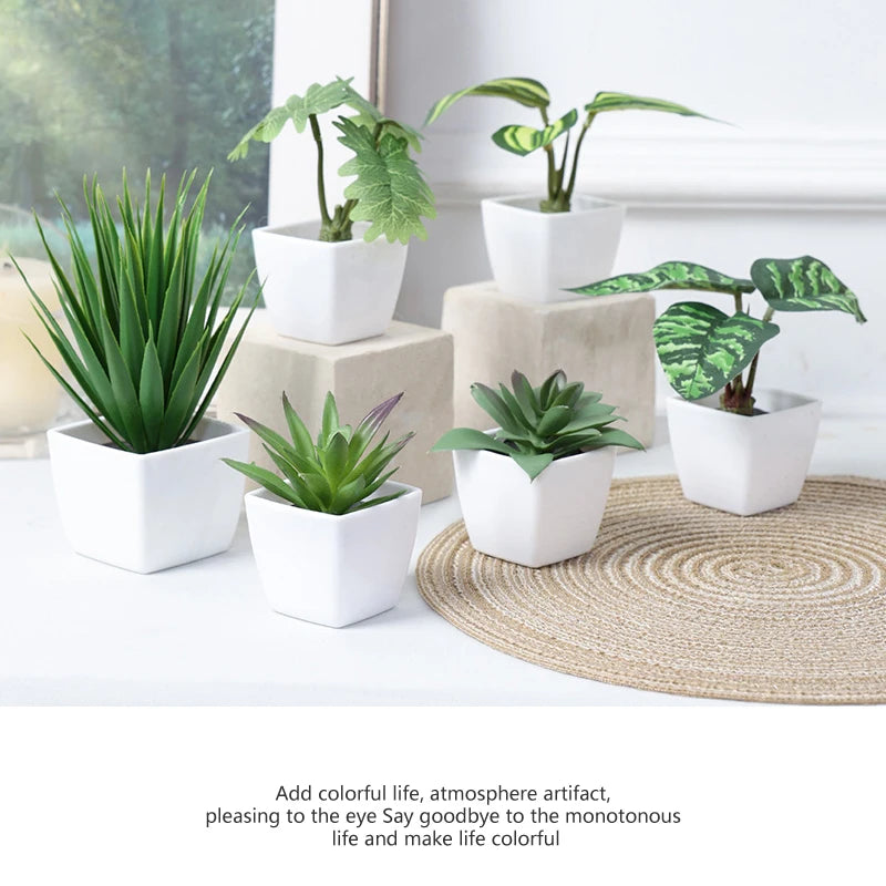A set of six small artificial green plants in white pots displayed on a light surface with a woven mat.