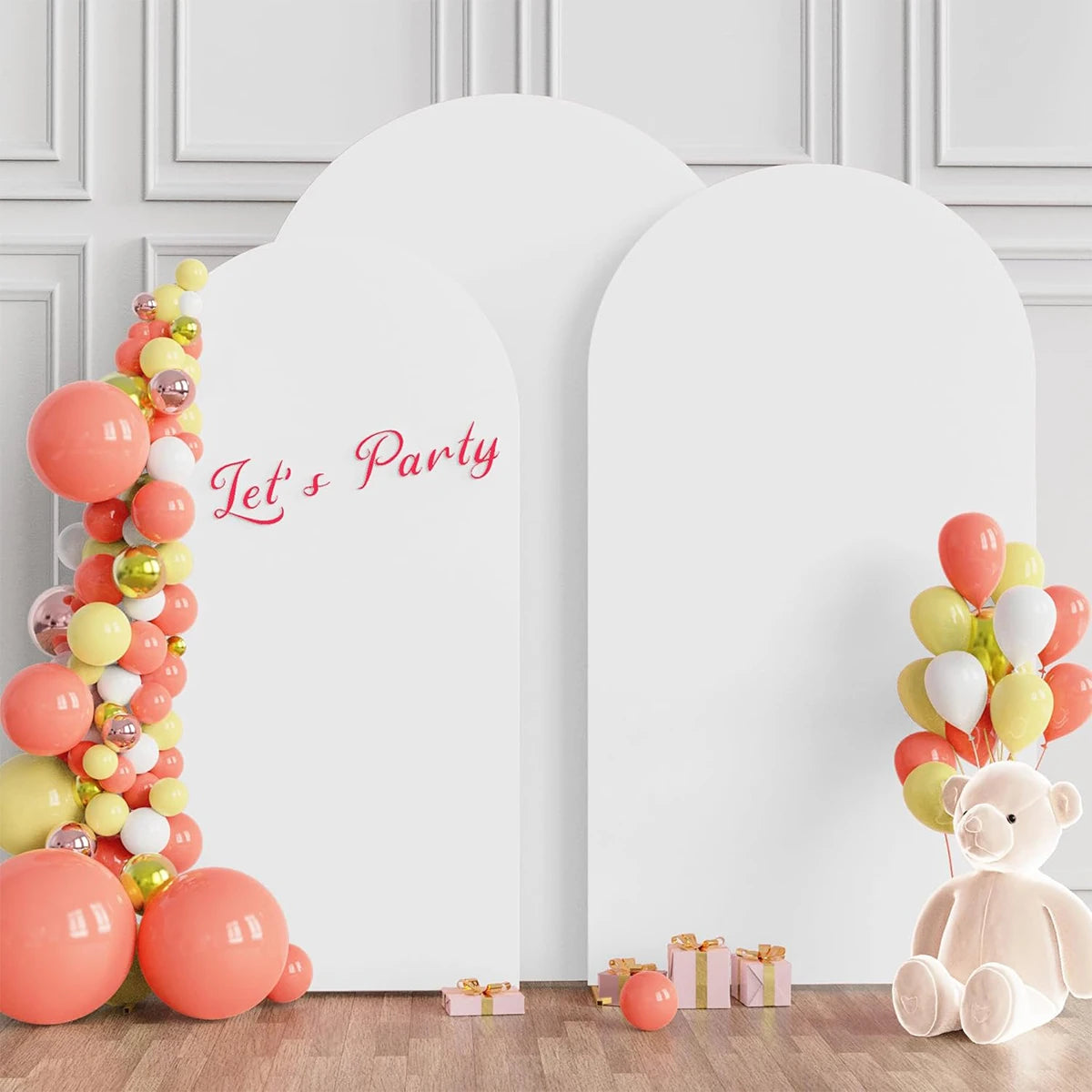 A white wedding arch cover decorated with pink and gold balloons and a teddy bear, set against a light gray wall.