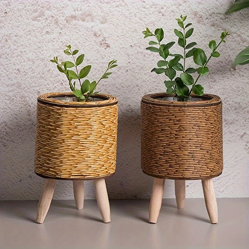 A rustic rattan planter with a small green plant sits on wooden legs against a light background.