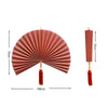 Handwoven bamboo wall fan decor in dusty rose color with a tassel hanging from the center.