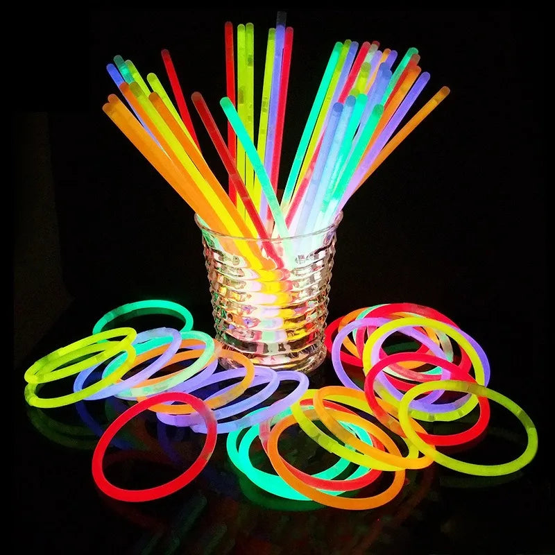 A glass filled with colorful glow sticks and flexible party bracelets arranged vertically and spread out on a dark surface.