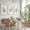 Three framed watercolor botanical prints featuring wildflowers and greenery displayed on a wooden table.