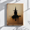 Minimalist witch silhouette wall art featuring a black witch figure on a broomstick against a warm, muted background.