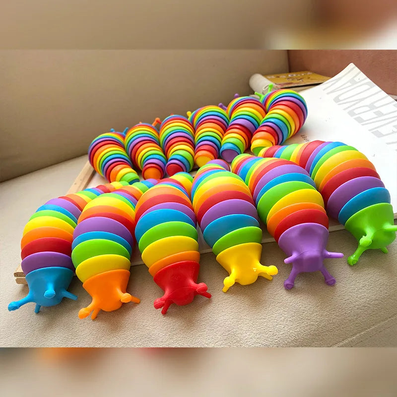 A colorful, flexible 3D articulated fidget slug toy arranged in a rainbow gradient on a light surface.