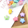 A collection of colorful decorative pentagram thumb tacks in various shades are displayed on a white surface next to a clear 