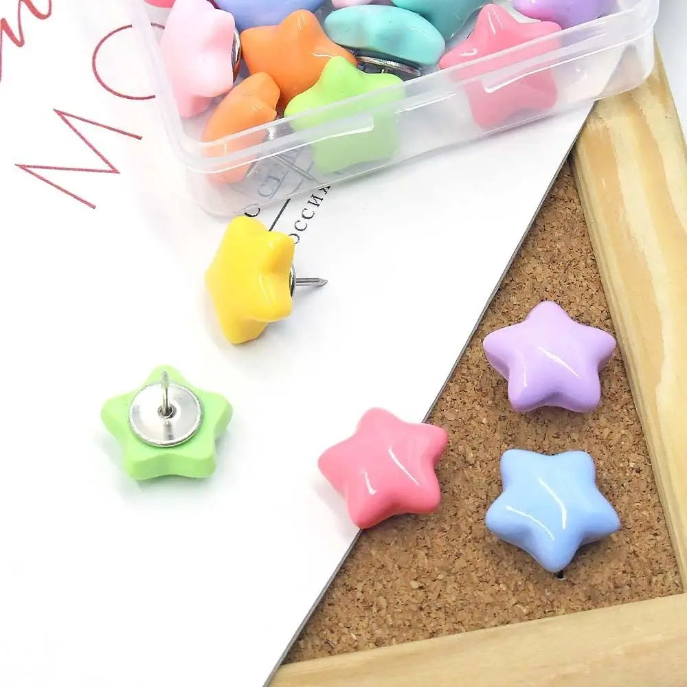A collection of colorful decorative pentagram thumb tacks in various shades are displayed on a white surface next to a clear 