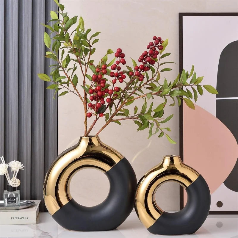 A pair of black and gold ceramic flower vases with green foliage are displayed on a white surface.