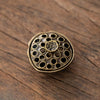 A vintage brass alloy incense burner holder with multiple small holes and a central decorative element resting on dark wood.