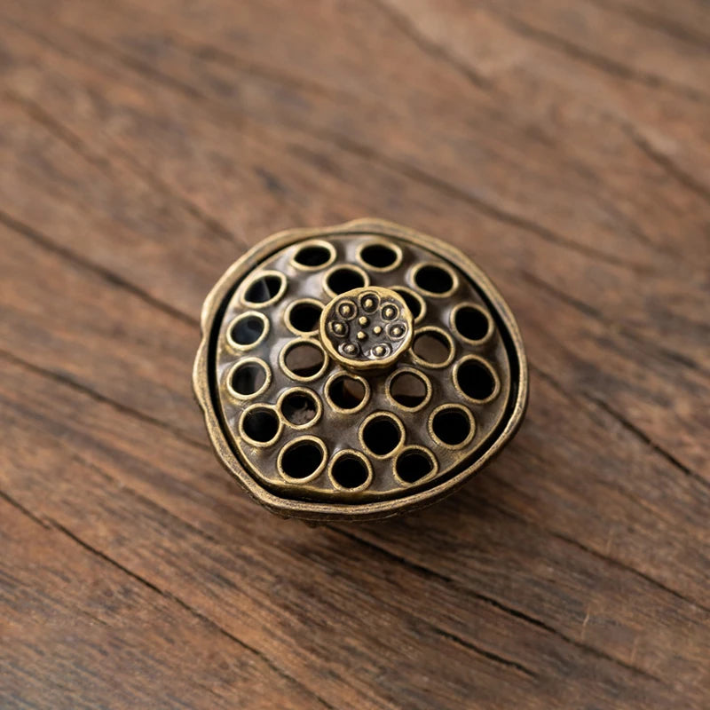 A vintage brass alloy incense burner holder with multiple small holes and a central decorative element resting on dark wood.