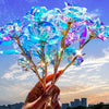 A hand holds a vibrant iridescent gold foil rose with blue and purple petals against a sunset sky.