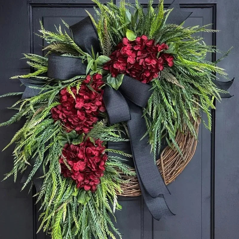A rustic wreath of green fir and deep red hydrangeas tied with a black ribbon, displayed on a dark door.