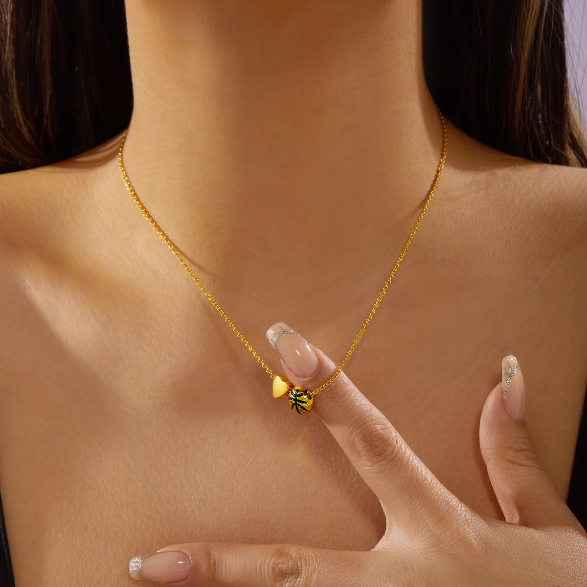 Gold heart basketball pendant necklace worn on a woman's neck and hand.