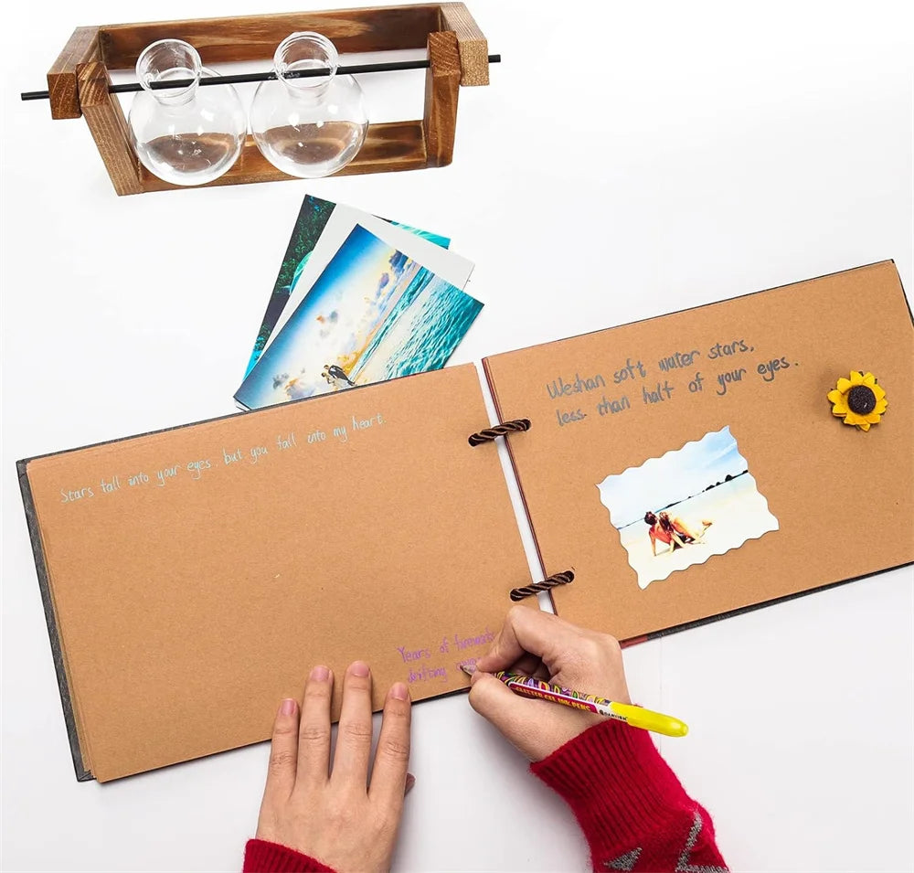 A hand is writing in a brown kraft scrapbook album with photos and a wooden frame nearby.