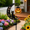 A black cat silhouette is featured on a metal crescent moon stake light with an orange pumpkin glass bulb in a garden setting