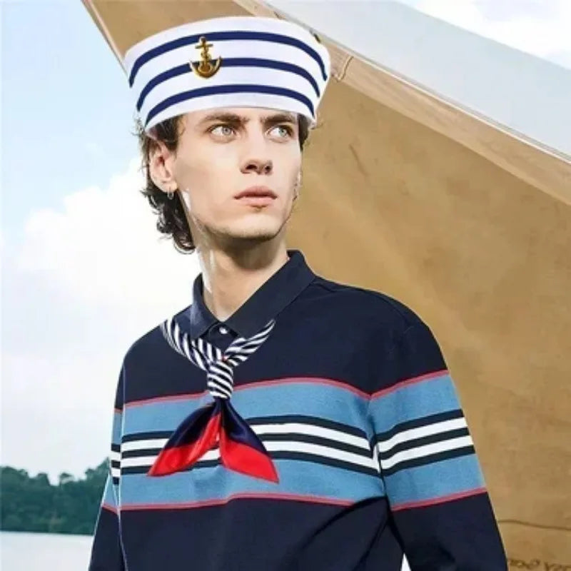 A male model wearing a navy blue striped shirt with a red scarf tied in a bow and a captain's hat.